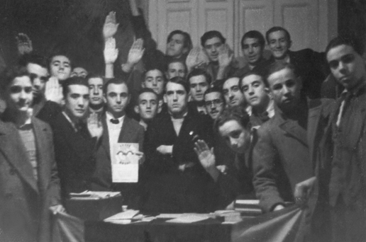 Ramiro Ledesma Ramos, en el centro de la imagen y con los brazos cruzados, en la sede de las JONS de Madrid rodeado de jóvenes militantes jonsistas. 